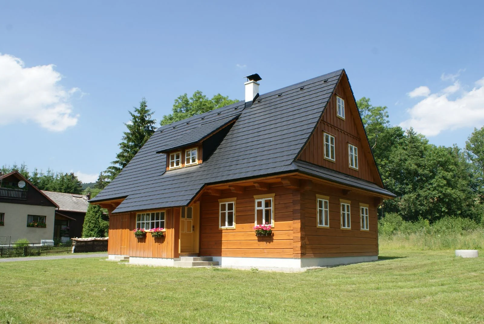 Menší dřevostavba, exteriér s dřevěným obkladem a muškáty v oknech